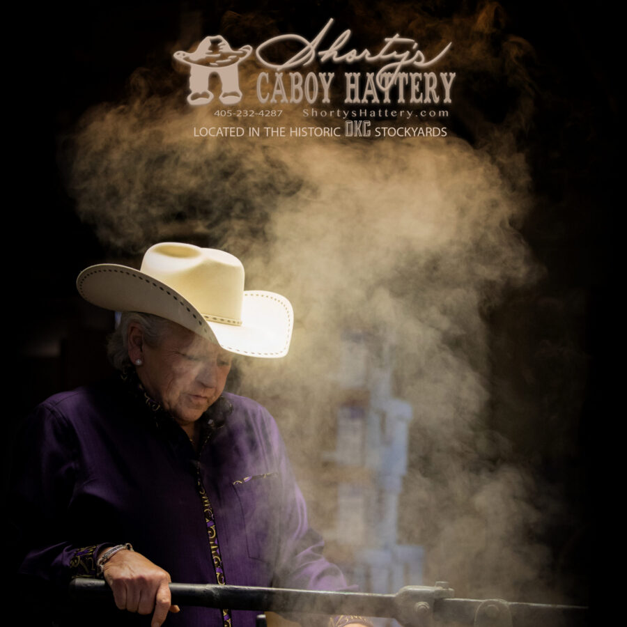 Photo of a woman wearing a white cowgirl hat with dust flying around her.