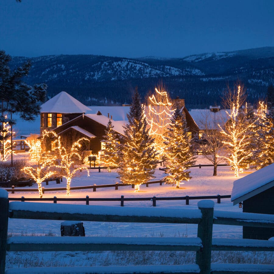 Barn and similar buildings covered in snow at night with white Christmas lights.