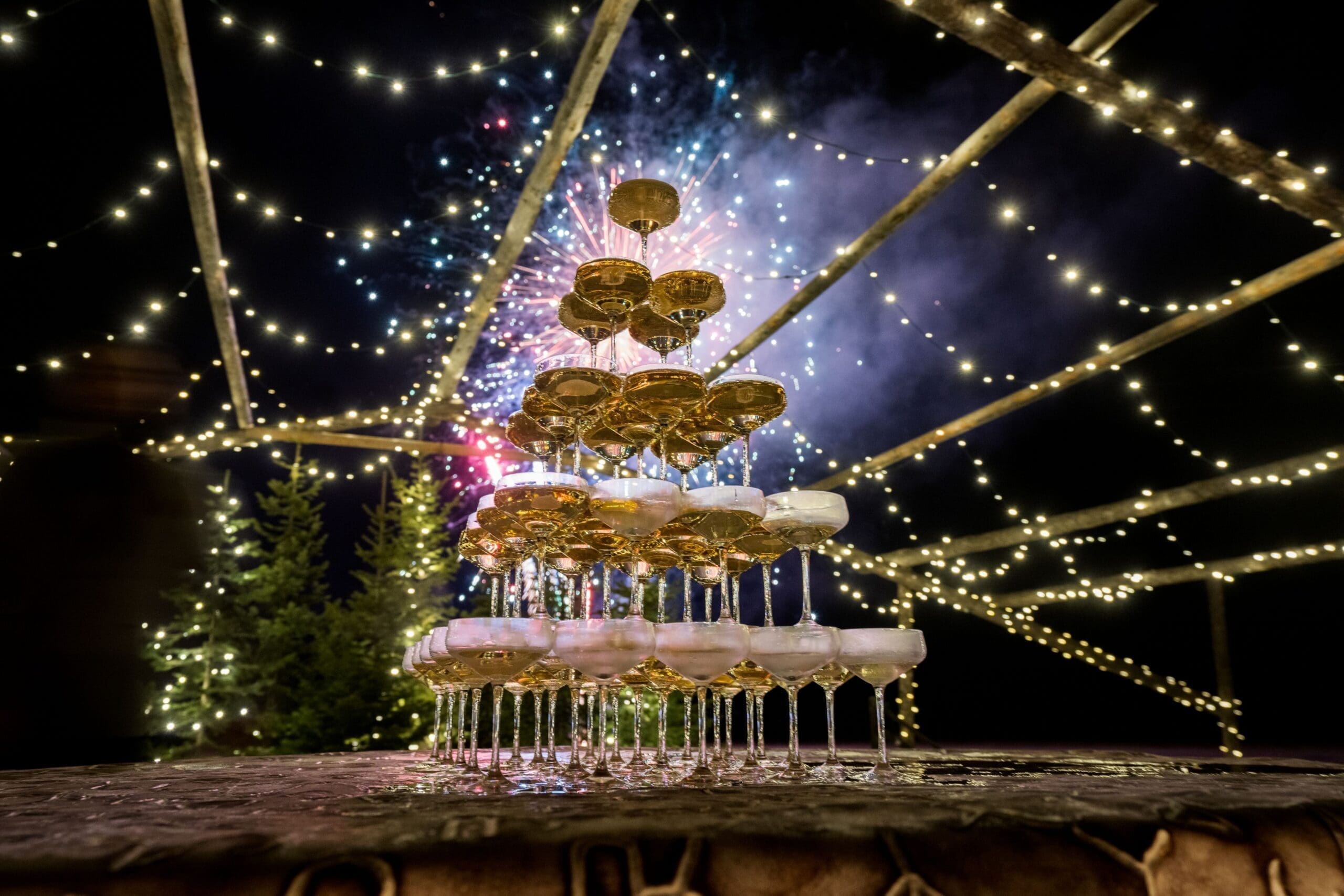 Champagne tower with fireworks in the background on New Year's Eve