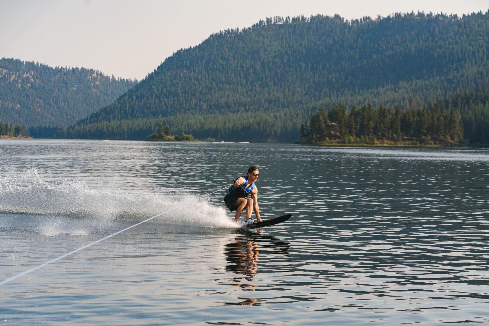Man on a skis in the middle of a lake with trees and hills in the background.