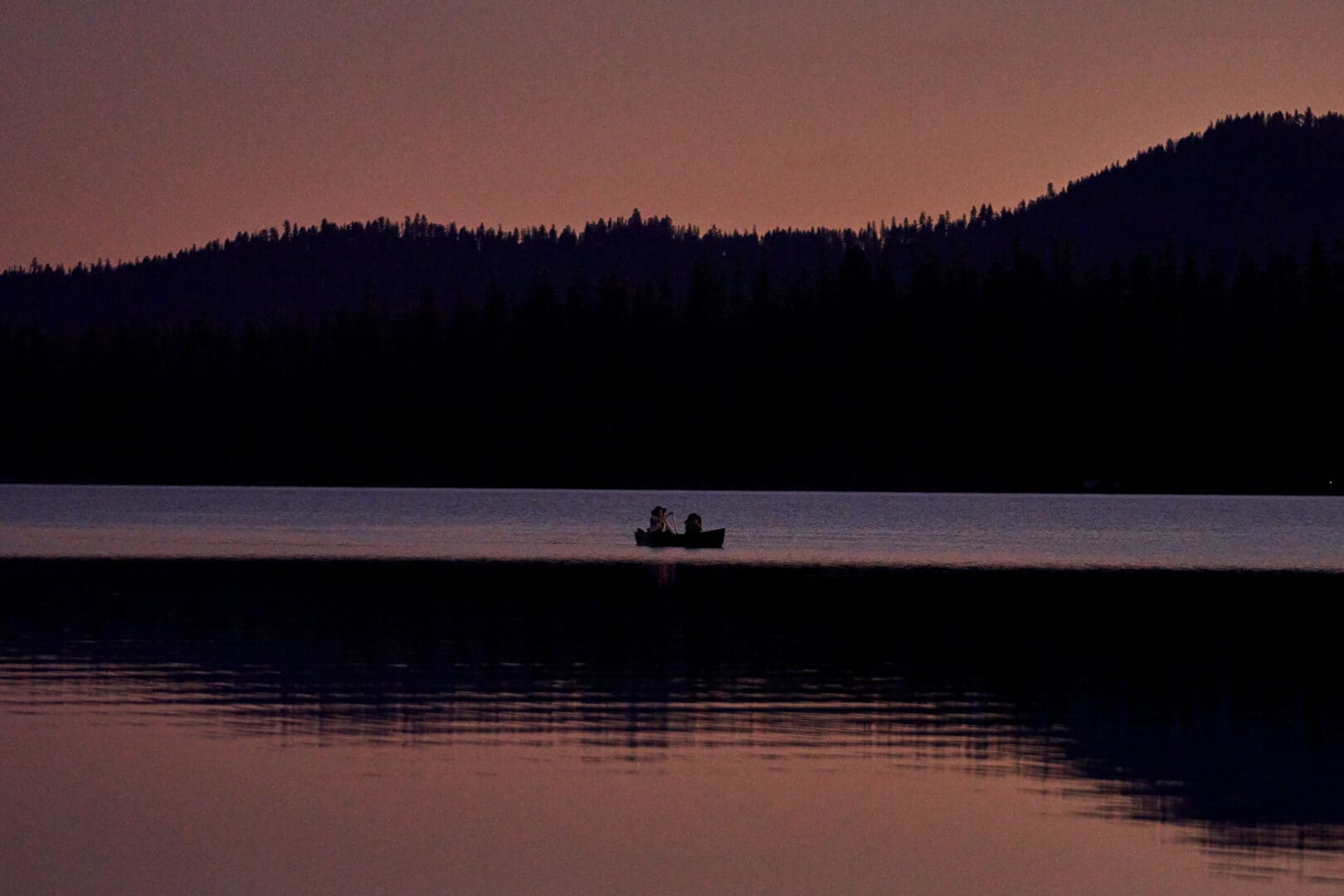 People in the distance paddling in a canoe on water during sunset.