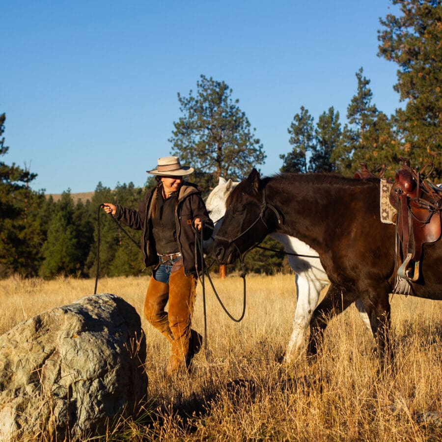 Woman leading two horses through a field.