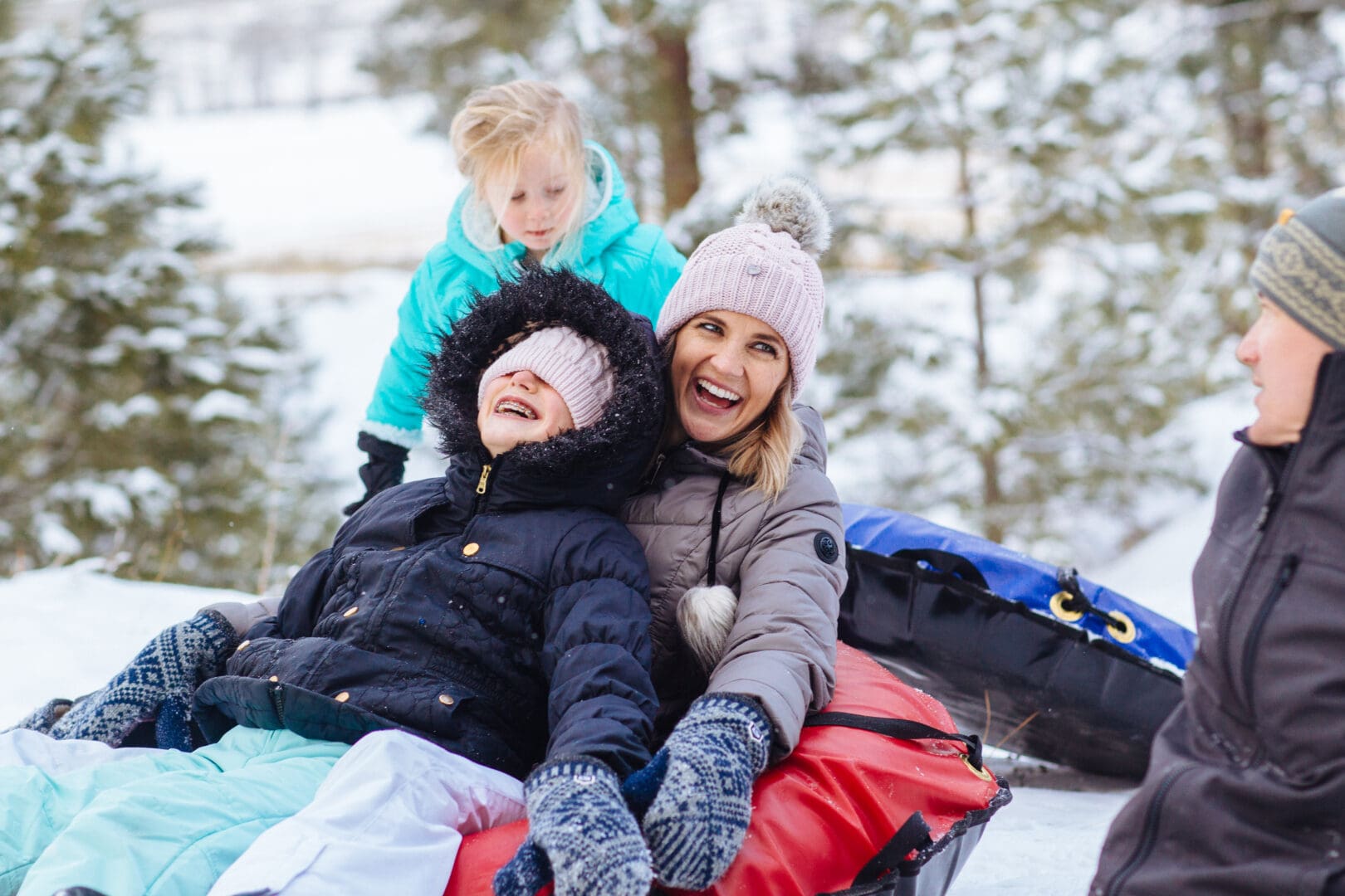 Family laughing and tubing down Blast Mountain snow hill at Paws Up