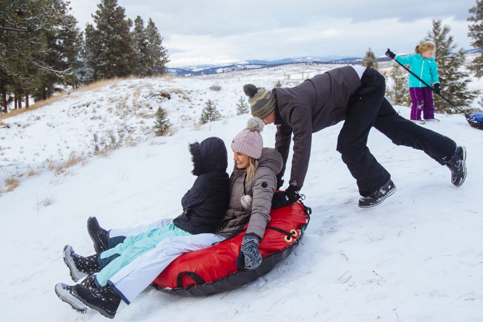 Mother and son getting pushed down a snow tubing hill on a red tube.