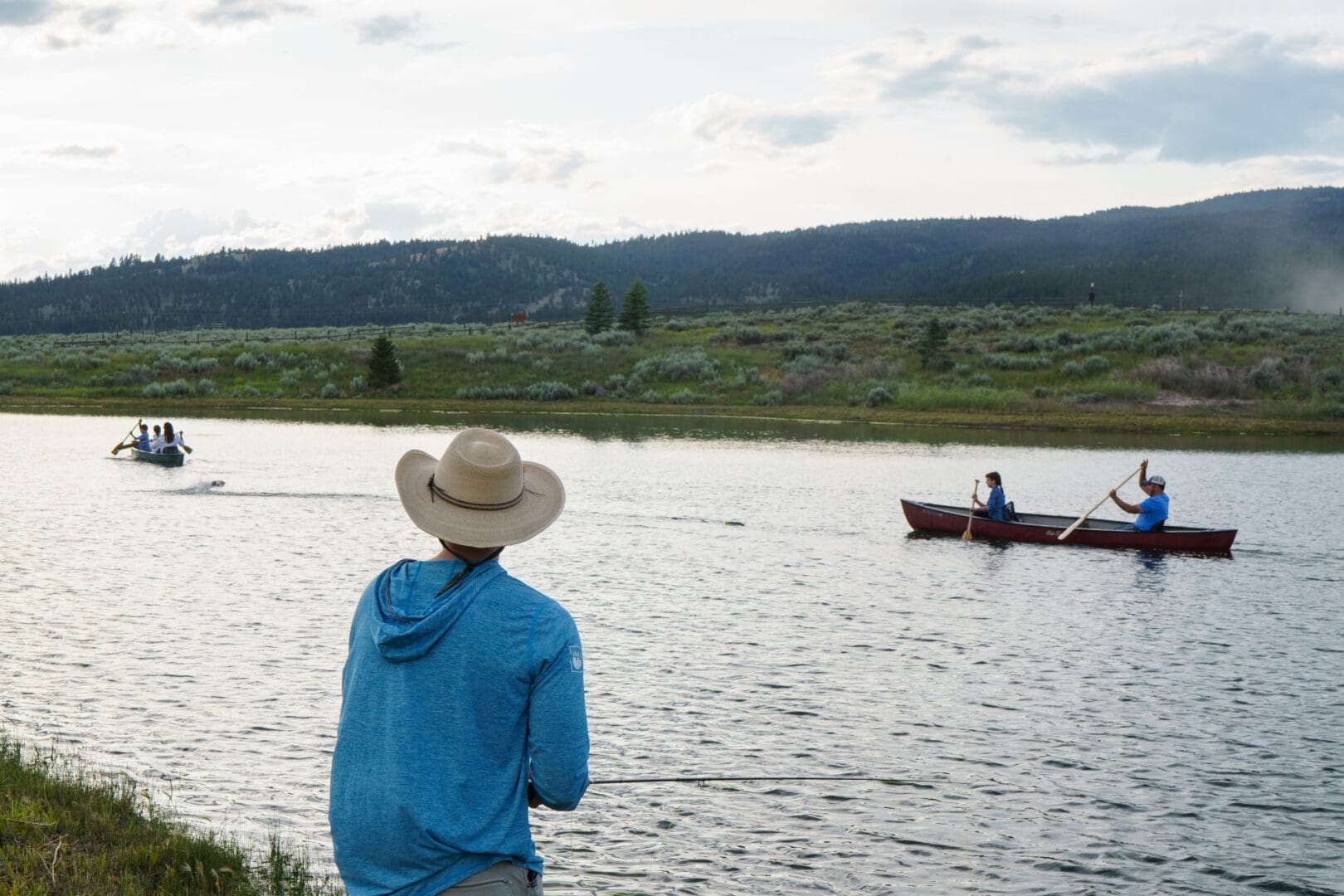 Man fishing with people paddling a canoe in the distance.