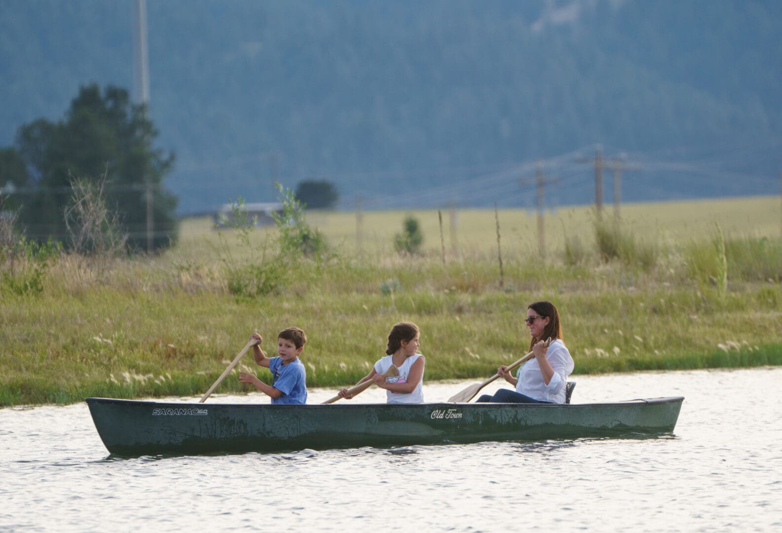 Mother and two children paddling in a canoe on water.