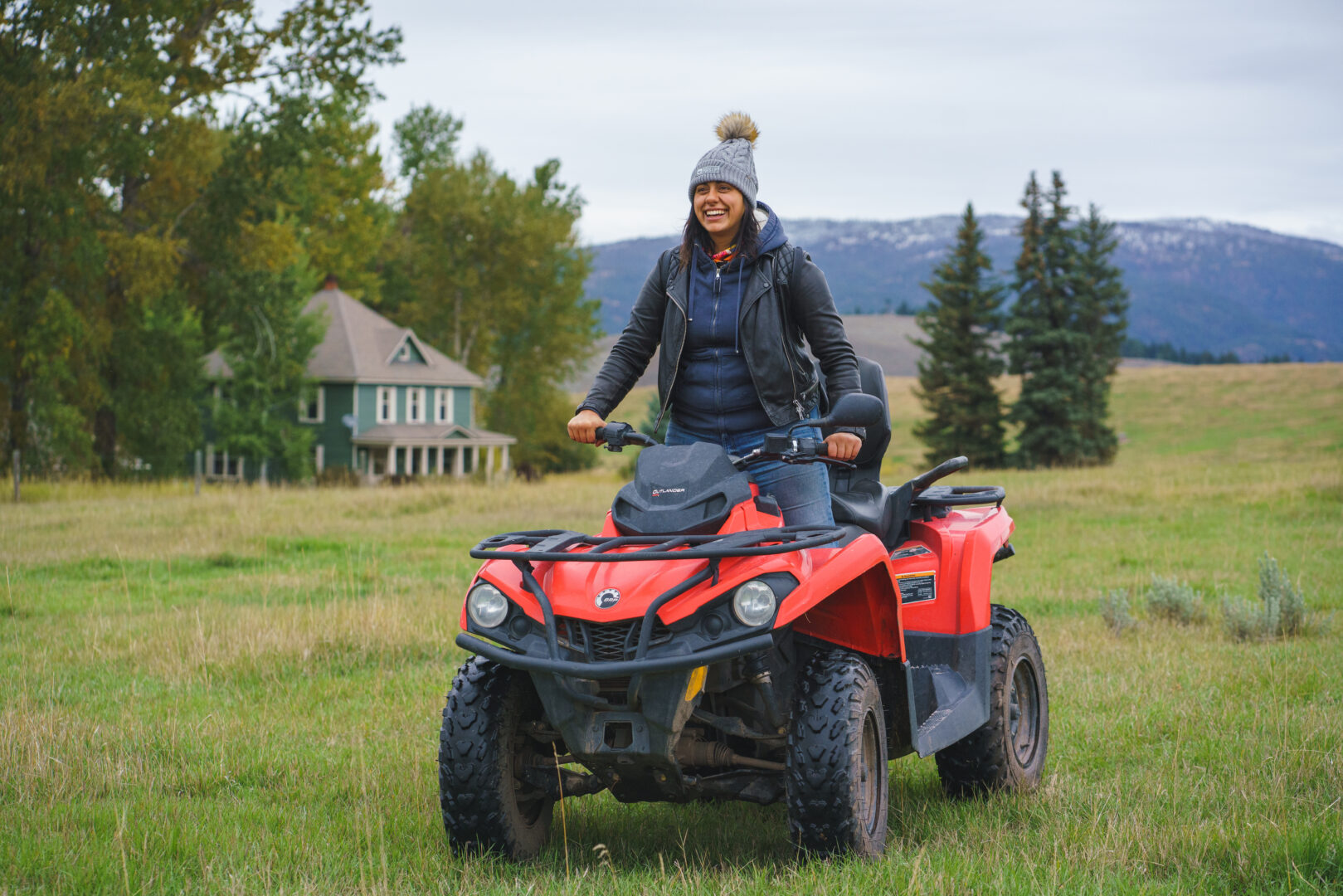 Woman sitting up on a red ATV with a house and green field behind her.