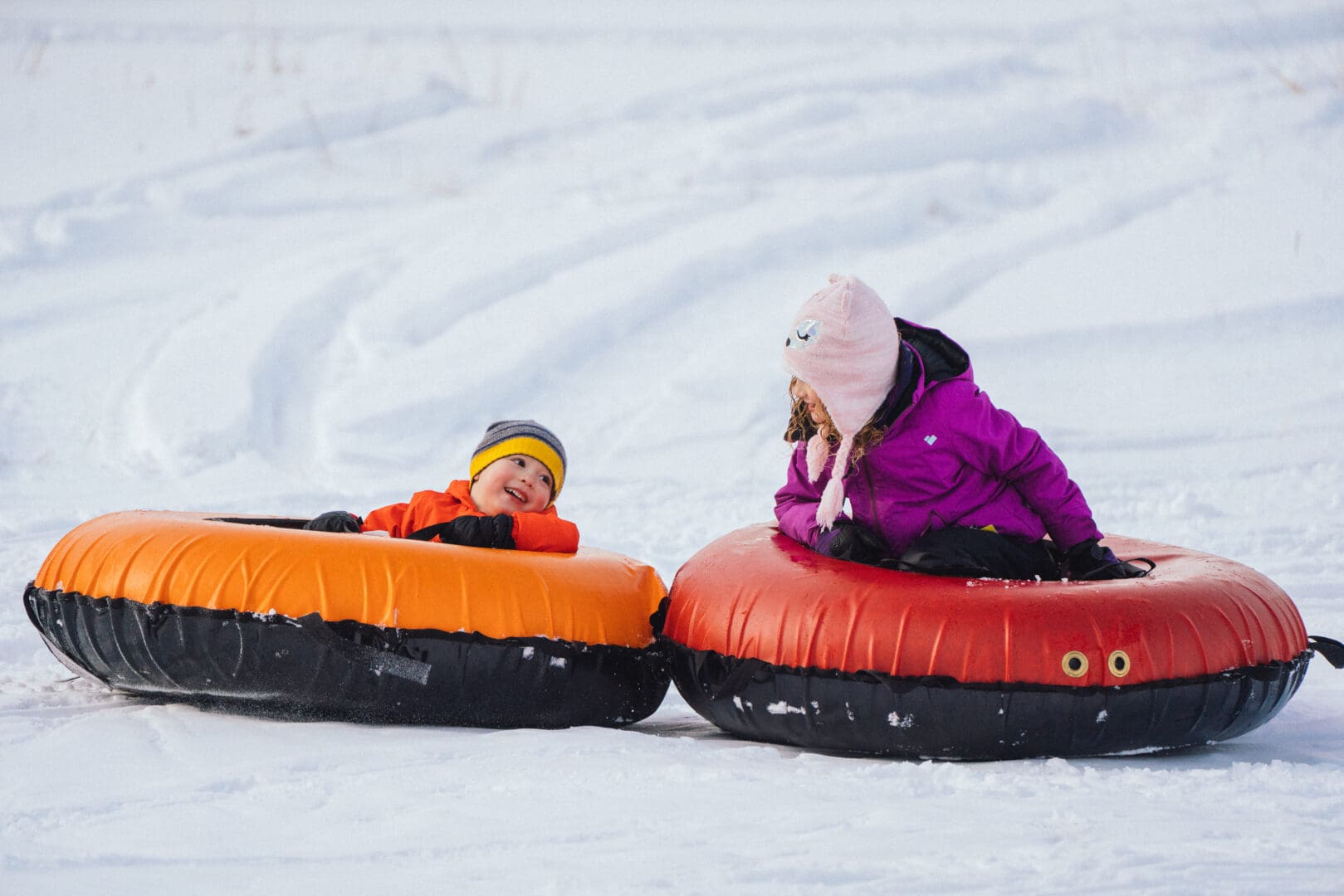 Two kids tubing down a snow hill.