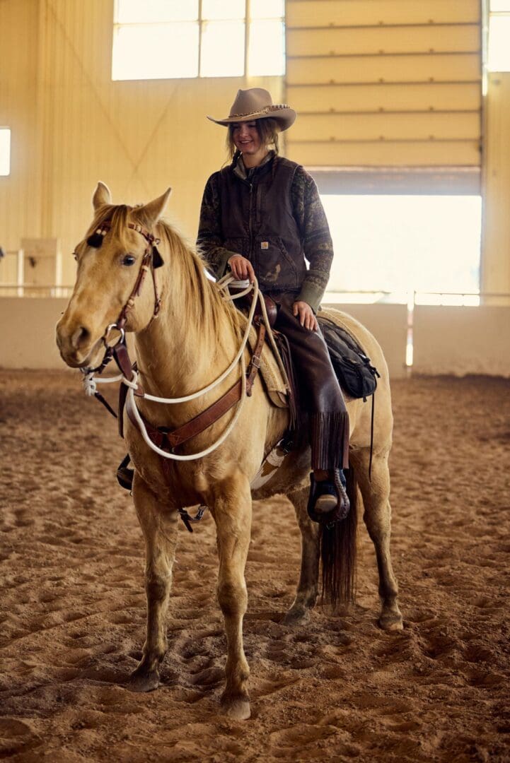 Person sitting on a horse wearing a cowboy hat in an arena.
