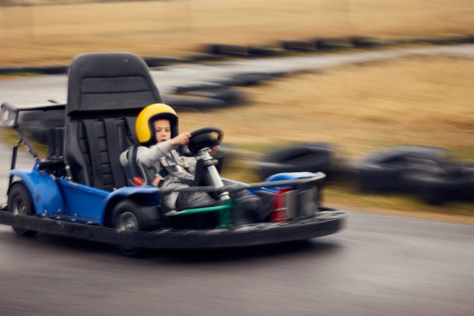 Little kid racing on an outdoor go-kart race track.