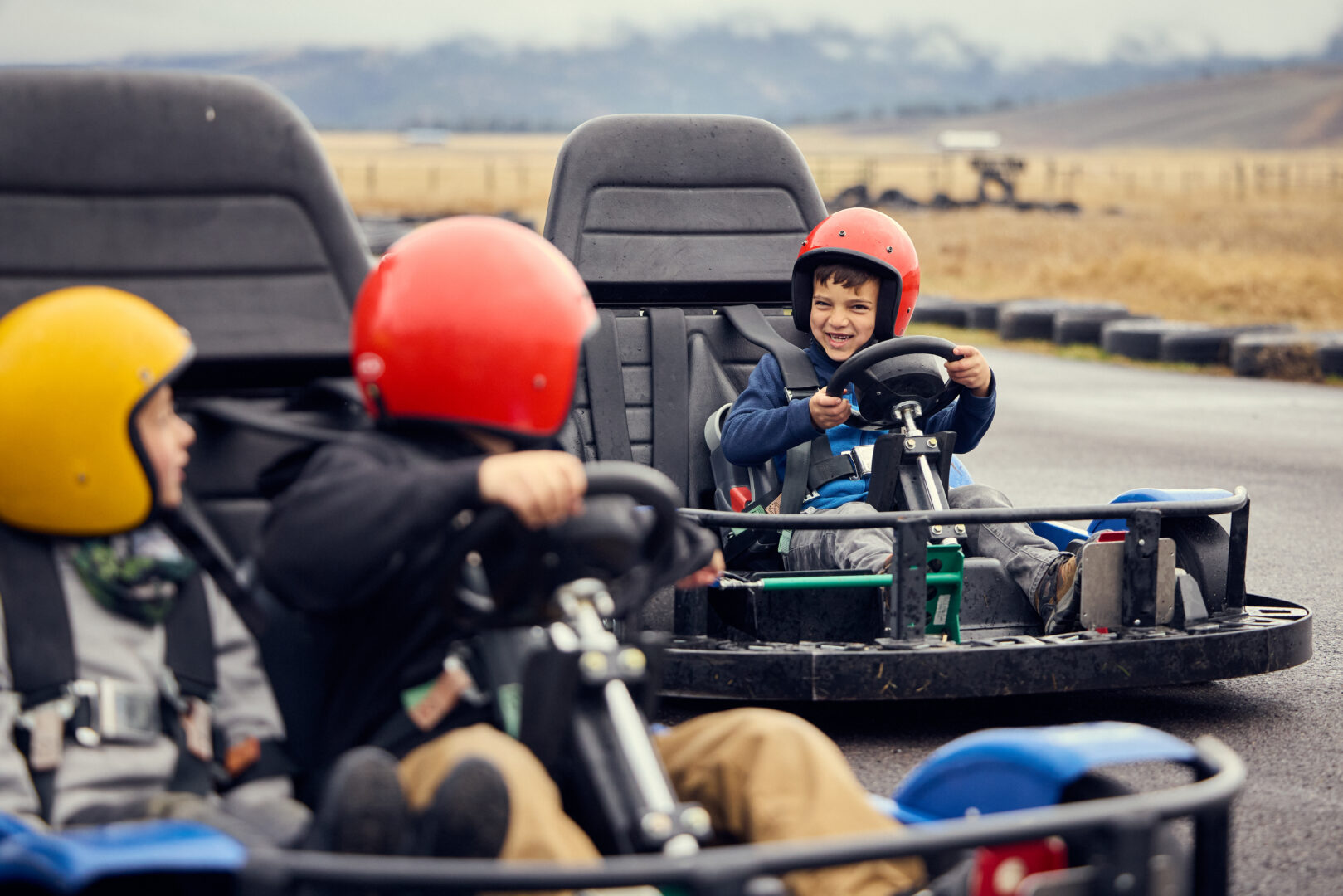 Three boys racing on go-karts on an outdoor track.