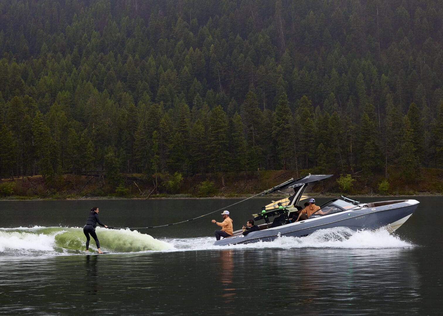 Woman on a wake board in the middle of a lake with trees and hills in the background.