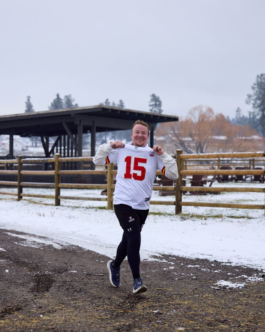 Man running with some snow behind him holding up a white and red football jersey that he is wearing.