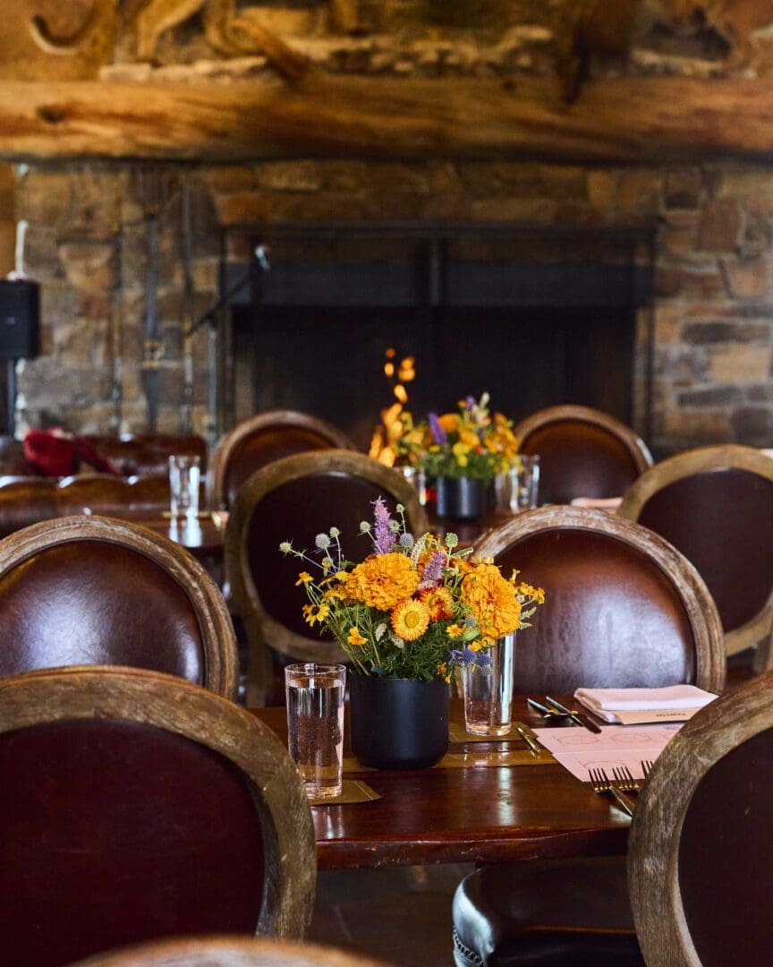 Inside of a dinning area with a stone fireplace and leather chairs.
