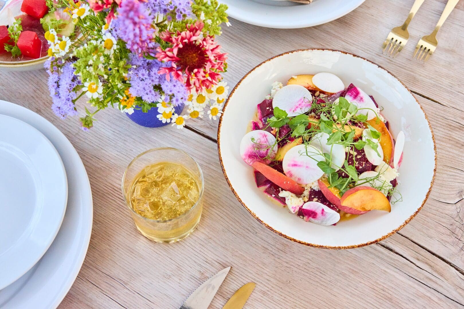 Fresh fruit salad on a plate with a cocktail and flowers beside it.
