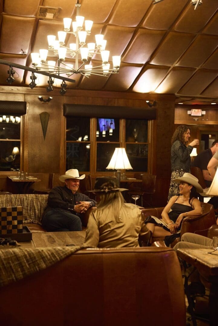Inside of a dimly lit bar area with people sitting on a leather couch holding cocktails.