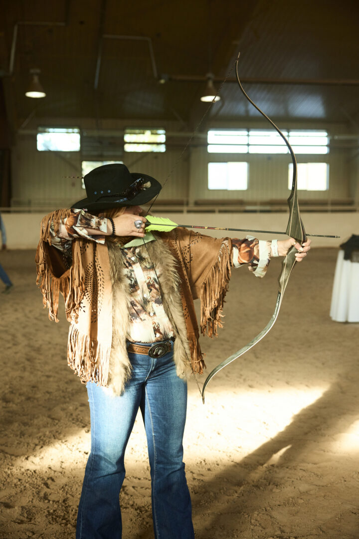 Woman shooting a bow and arrow inside of an arena.