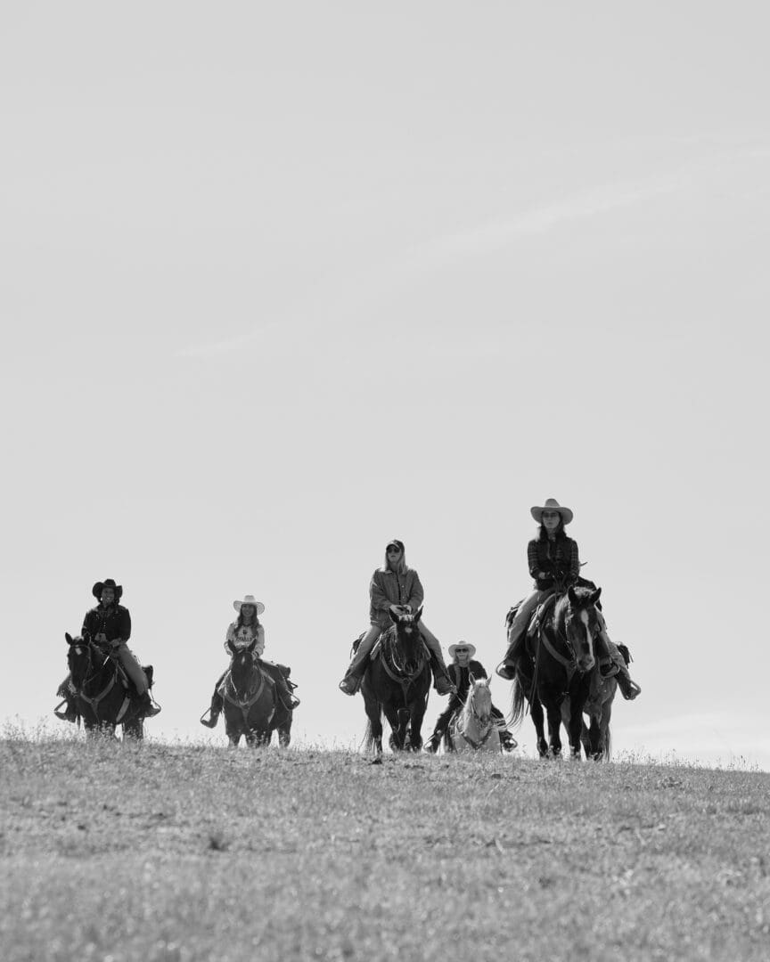Group of women riding horseback on a grassy hill in a black and white photo.