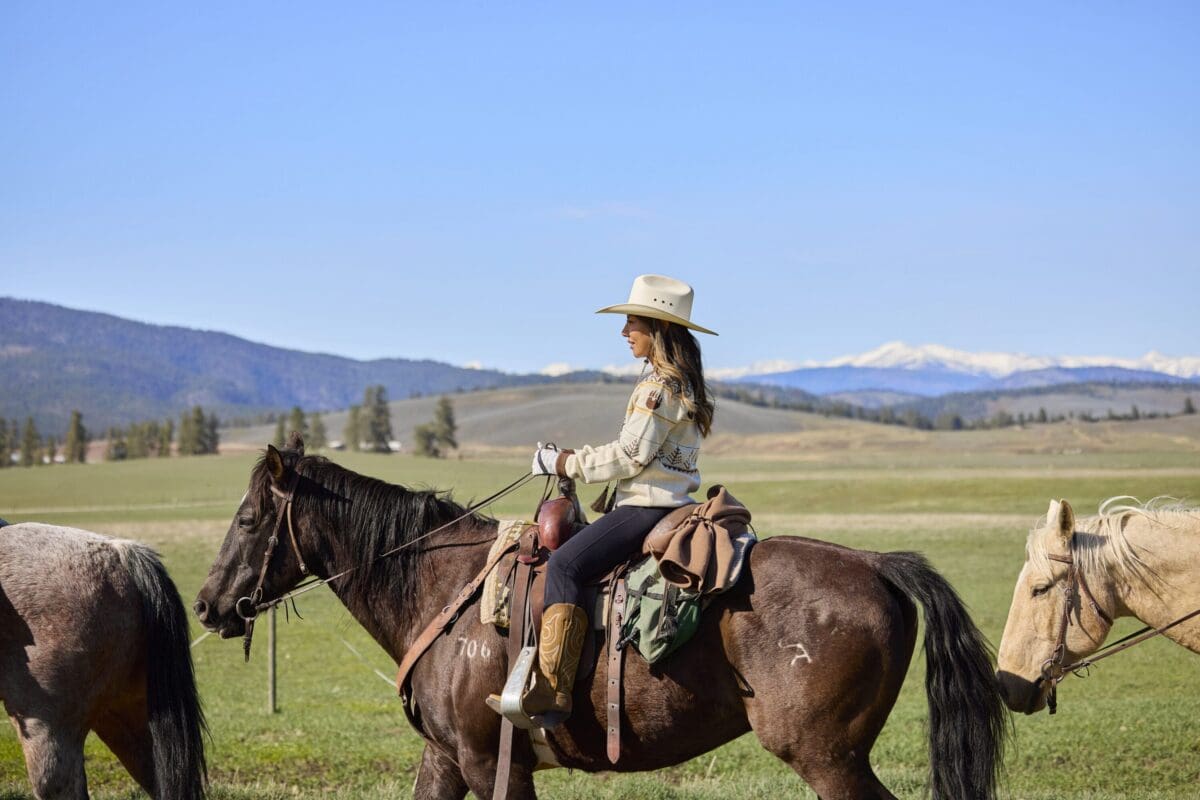 Woman sitting on a horse with mountains and green hills behind her.