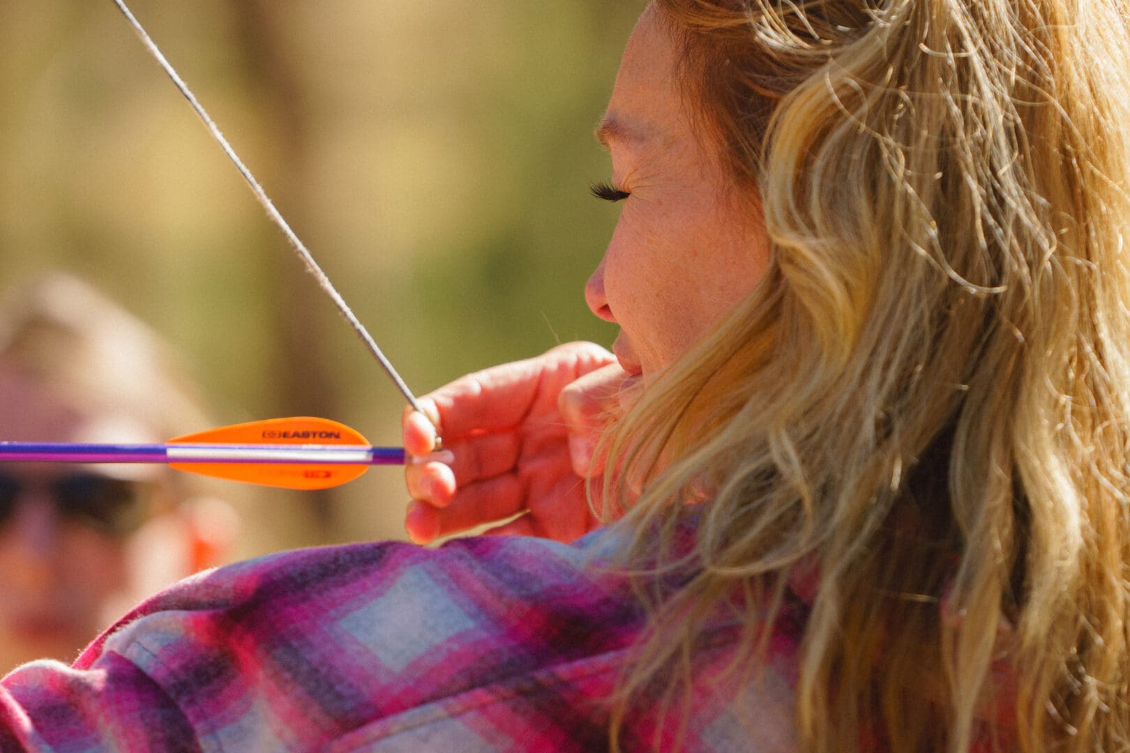 Woman shooting a bow and arrow in a forest.
