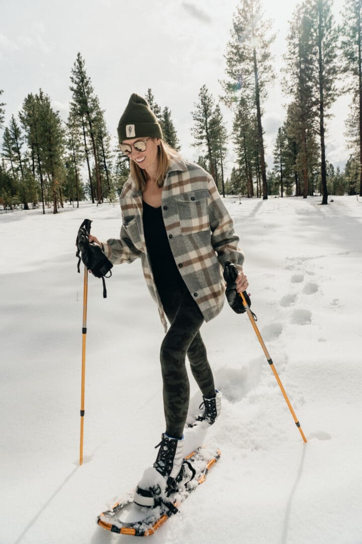 Woman walking through the snow in snowshoes and using walking poles.