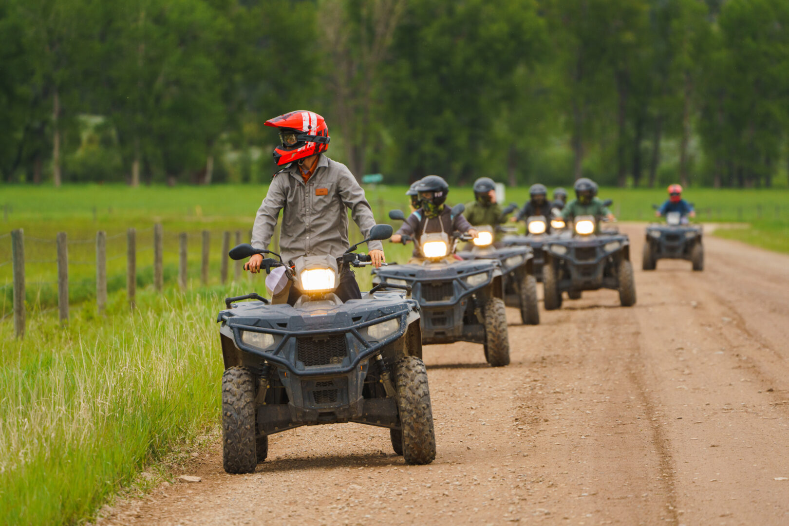 Series of people riding ATVs right behind each other on a dirt road.