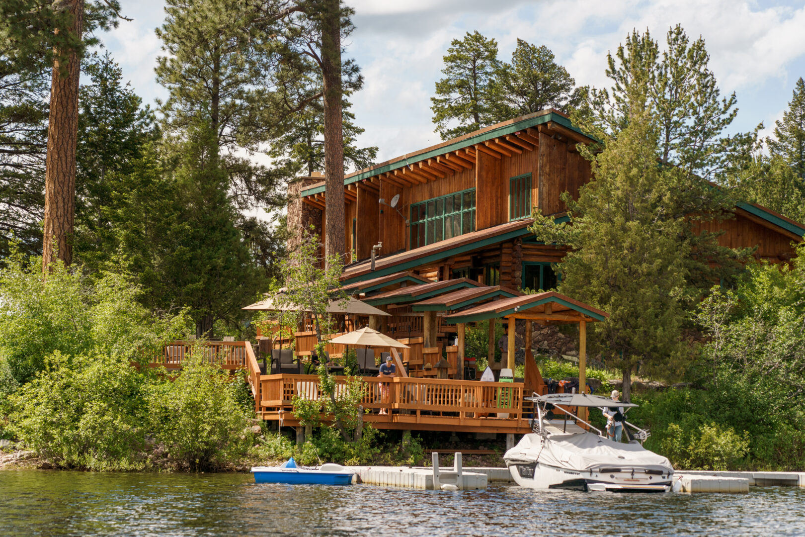 Wooden lodge on a river with boats and trees surrounding it.