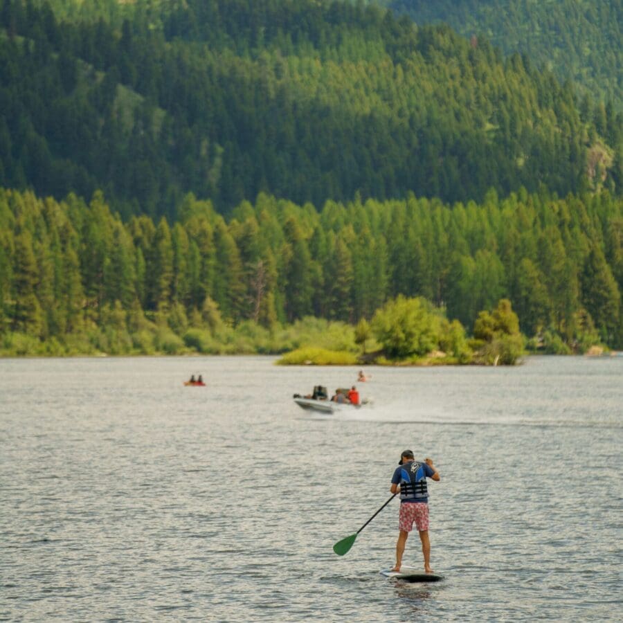 Man on a paddle board in the middle of a lake with trees and hills in the background.