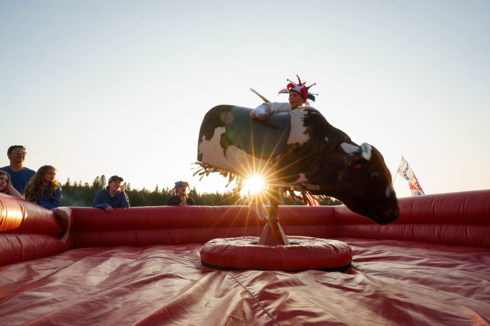 Kid riding a mechanical bull in a red blow up pen.