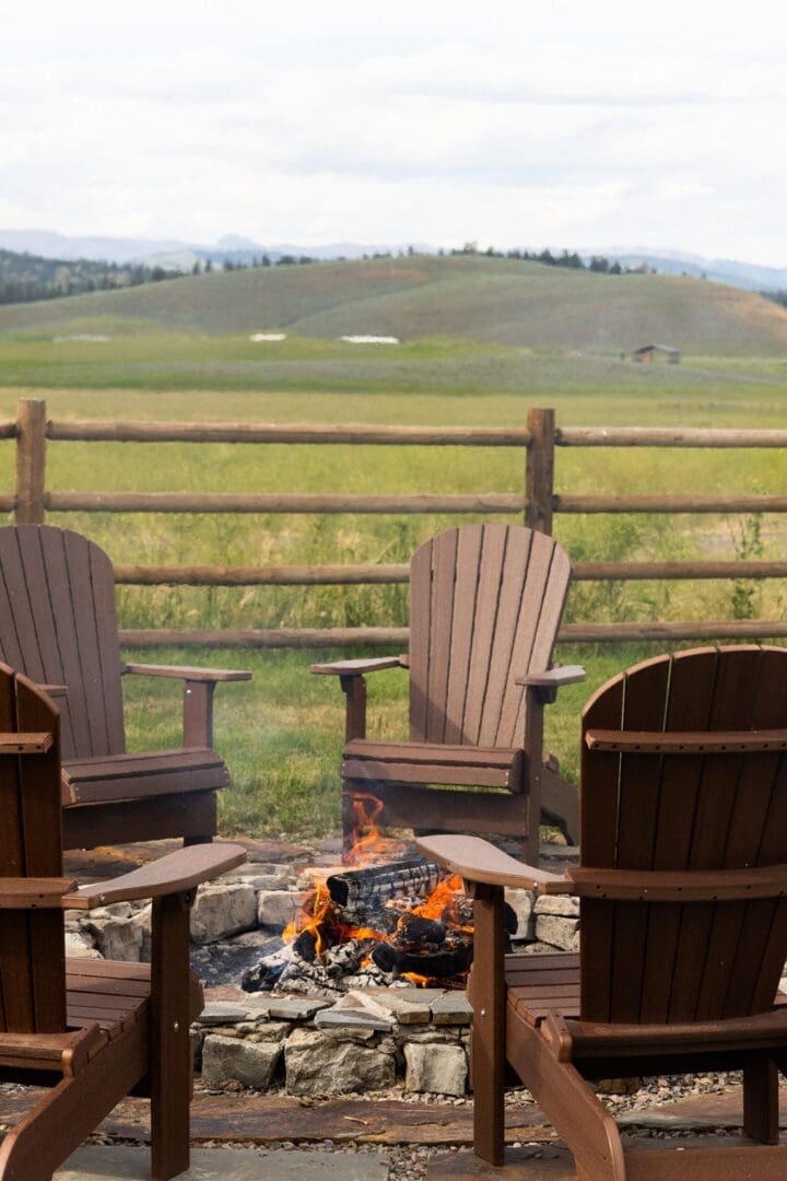 Chairs around a fire with a wooden fence post and large lawn behind it.