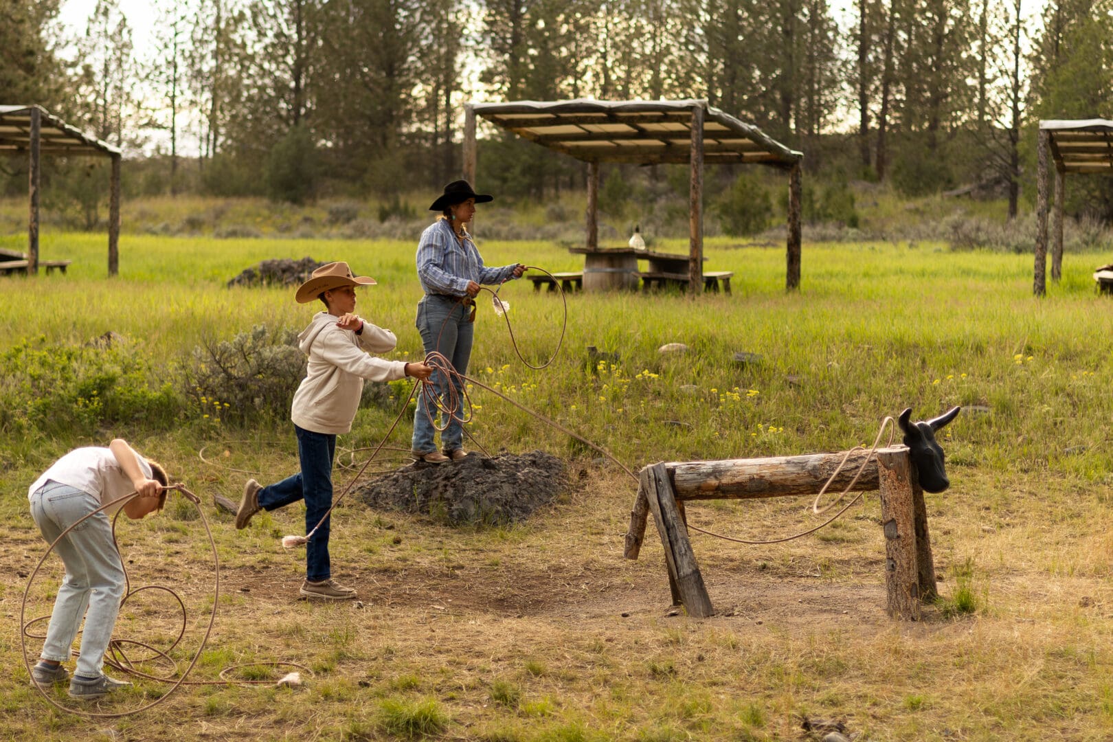 Three people lassoing a fake cattle.