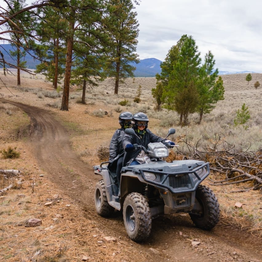 Two riders on a black ATV on a mountainous dirt road