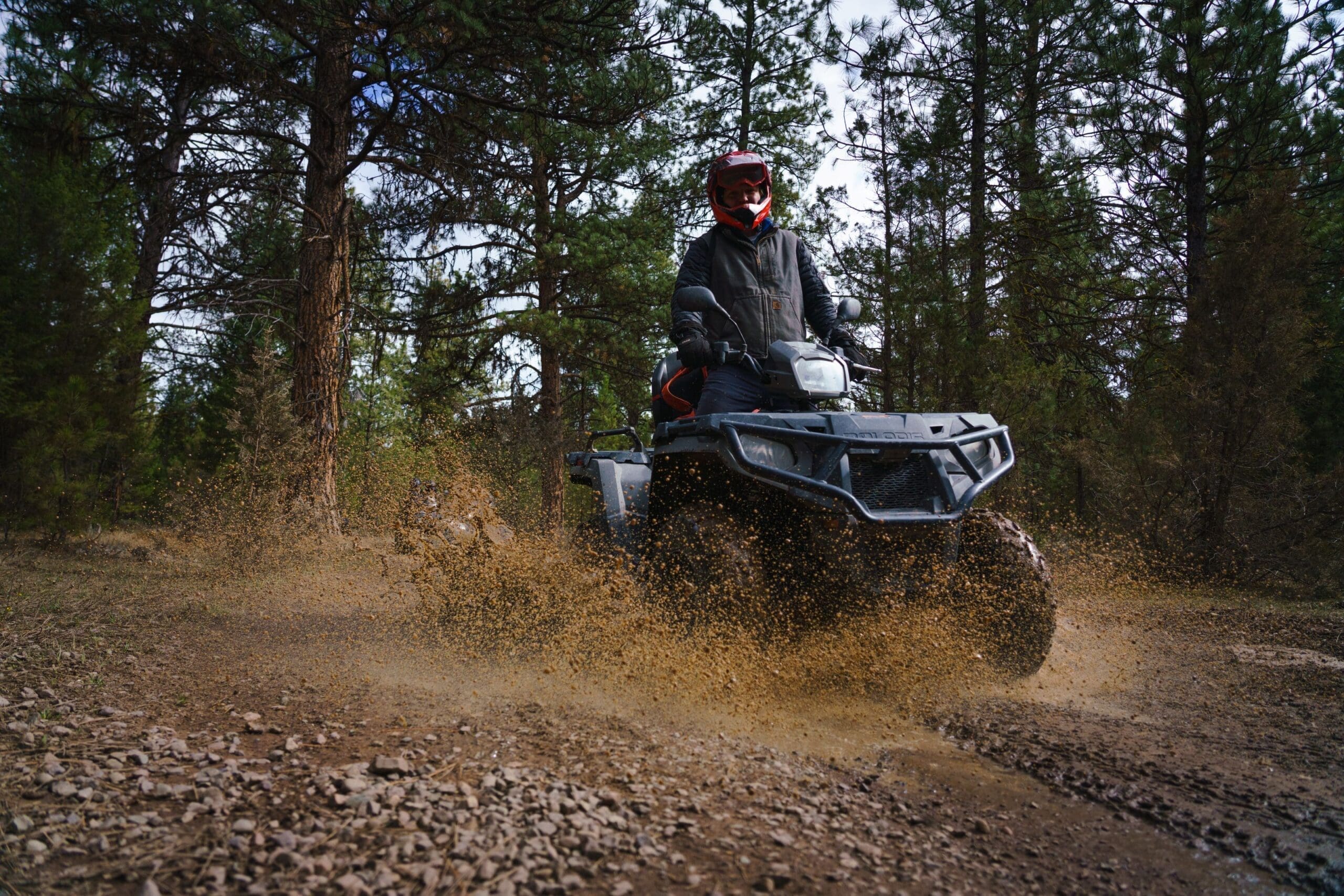 Driver riding an ATV through a muddy forest trail