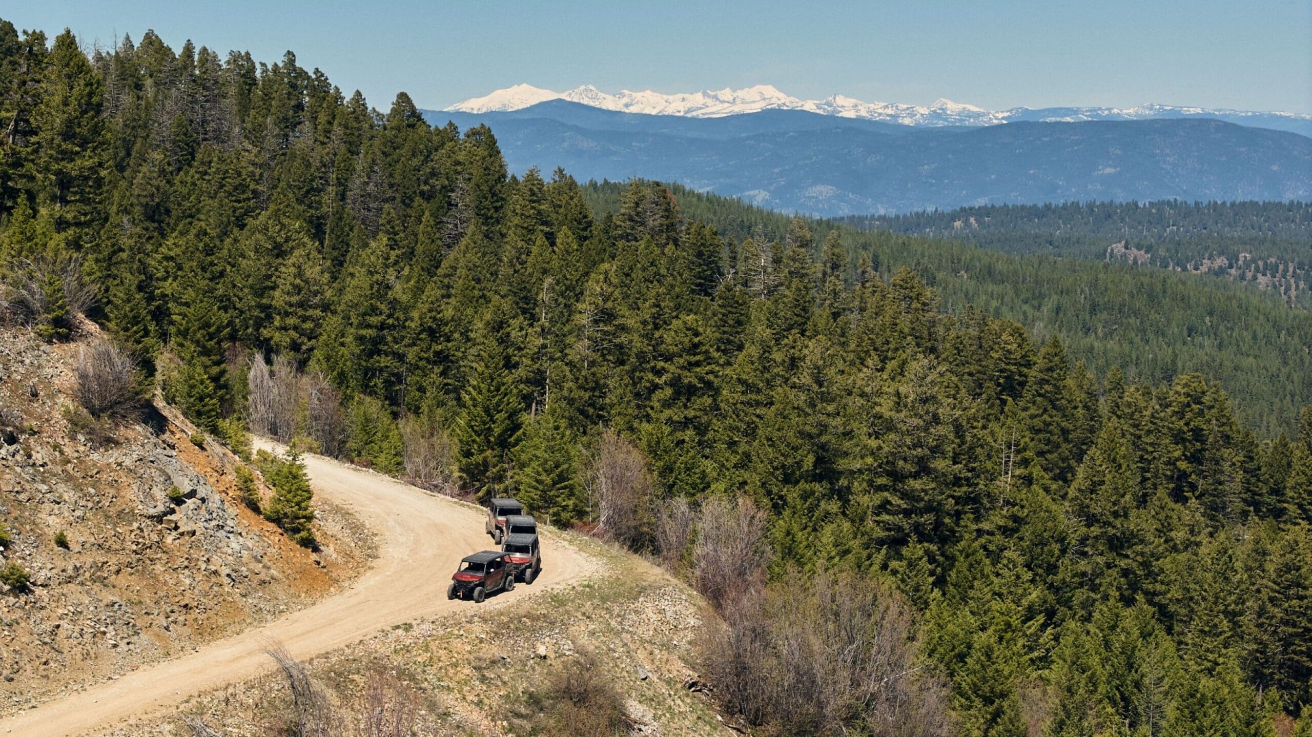 Wide view of UTVs driving on a dirt forest road in the mountains on a backcountry tour