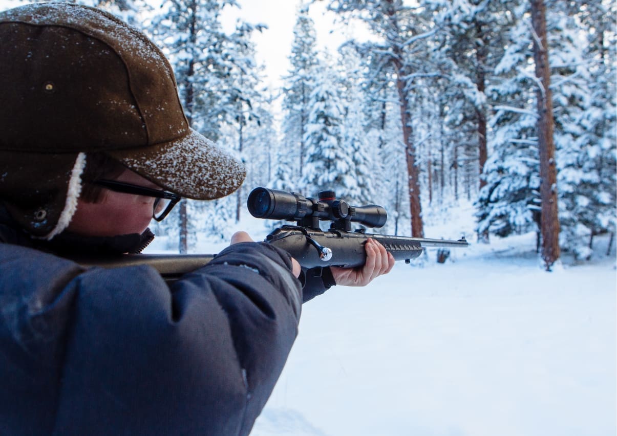 man in winter hat shooting rifle in snowy landscape for biathlon