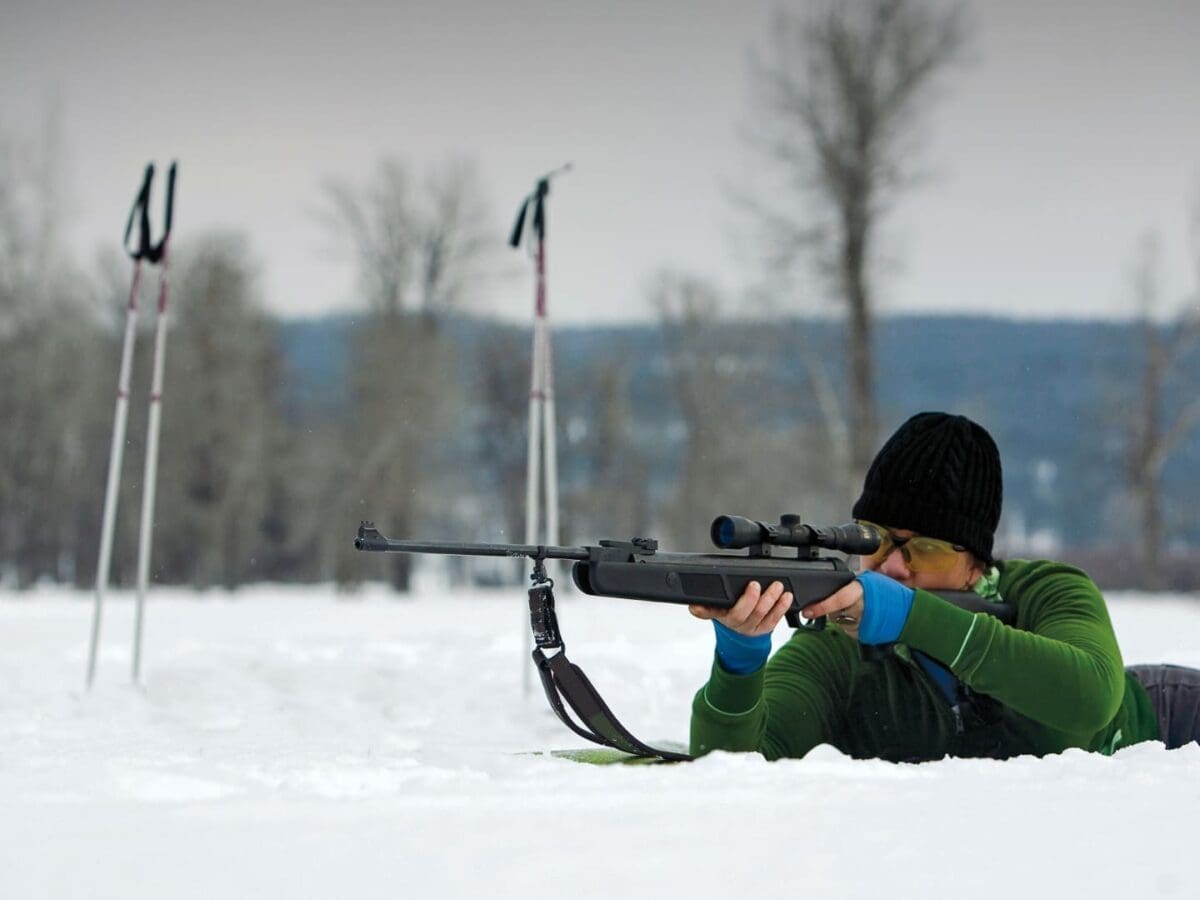 Woman laying in the snow shooting a rifle for biathlon