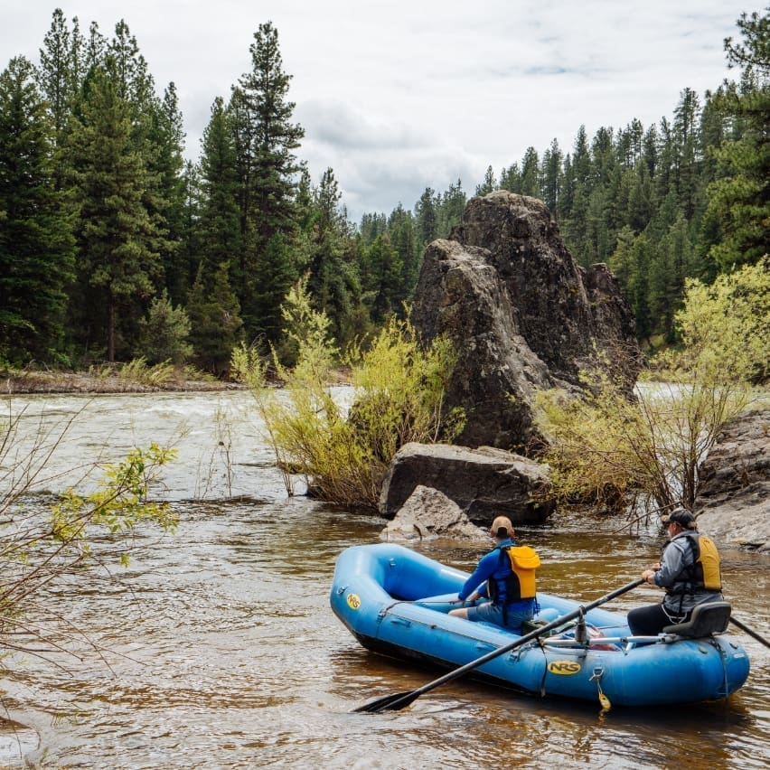 Two people paddling through the Blackfoot River in a blue raft