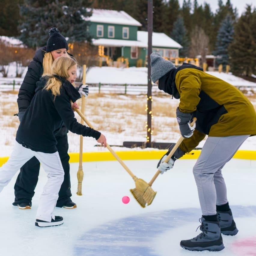 A family playing broom hockey on a skating rink at Paws Up