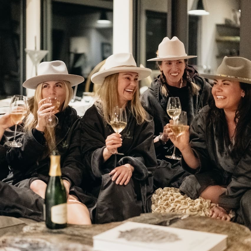 A group of women laughing and drinking wine together in matching pajamas