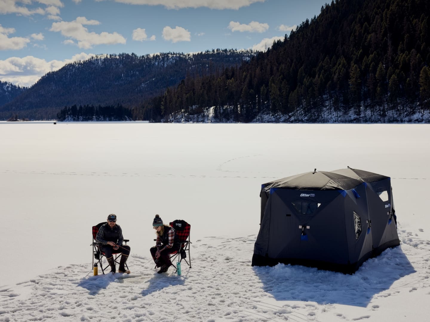 Two people sitting on a frozen mountain lake, ice fishing