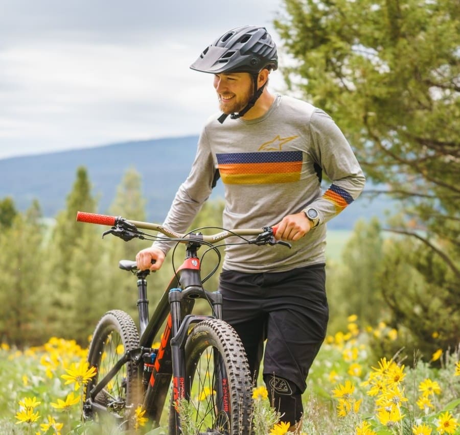Mountain biker standing next to his bike while enjoying the flowers and mountain view