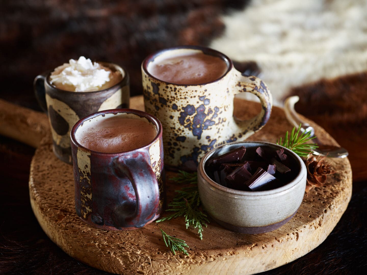 Hot chocolate in various mugs on a wooden board with chocolate shavings.