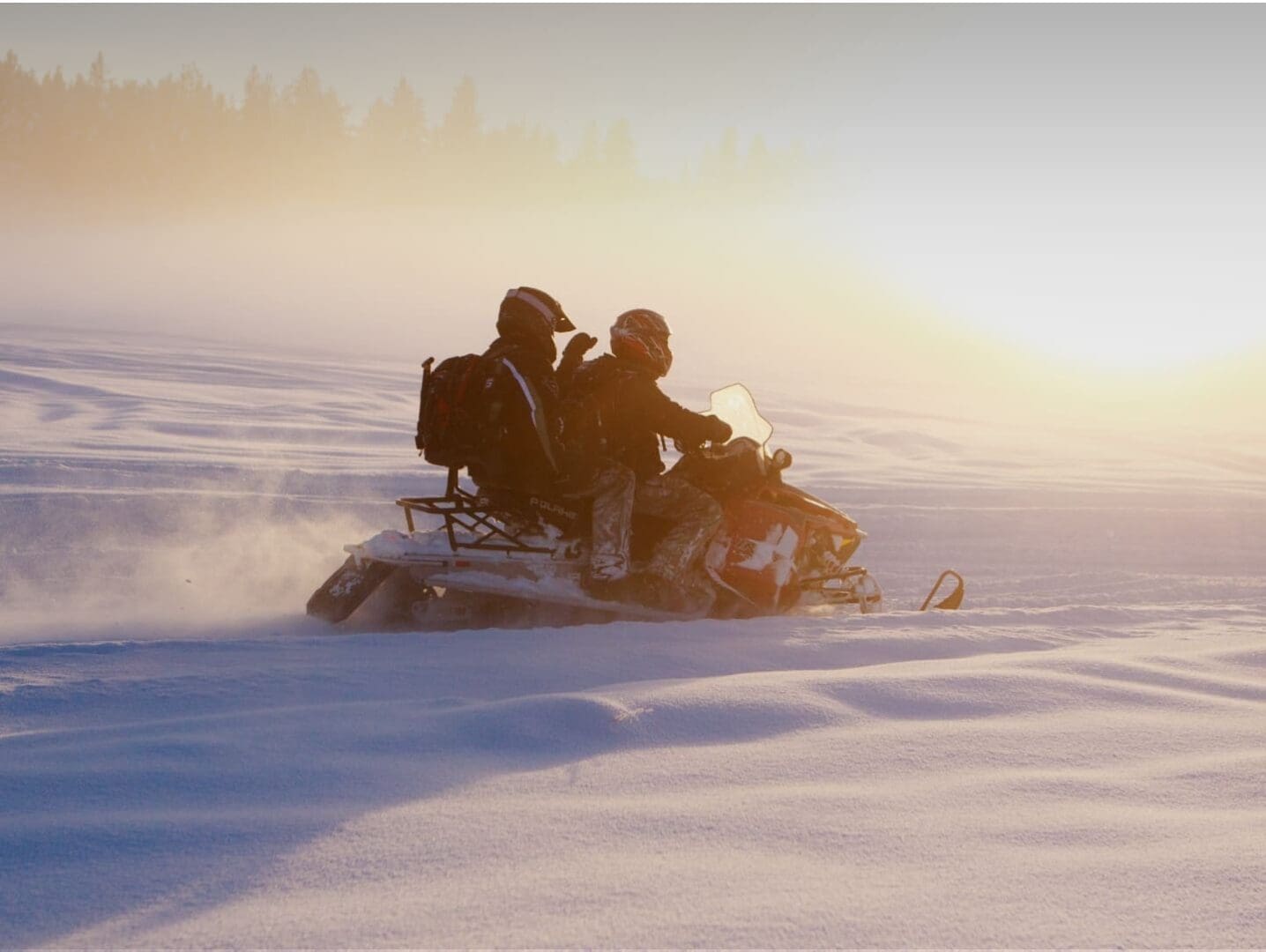 Two people riding in a snowmobile through a winter field