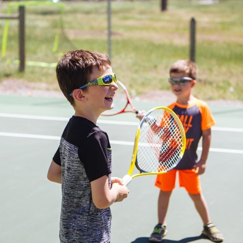 Two little boys playing tennis in the sun