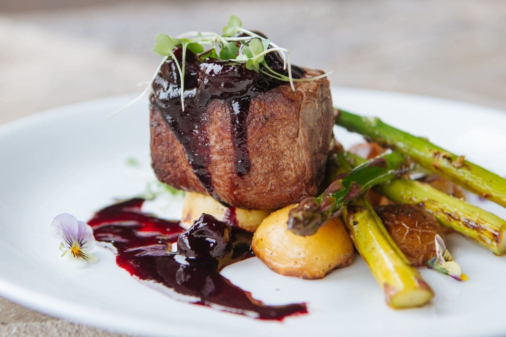 Steak dish with dark red sauce and potatoes and asparagus