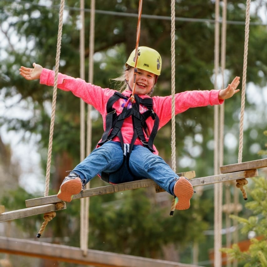 Little girl in a harness hanging from a rope in a ropes coure