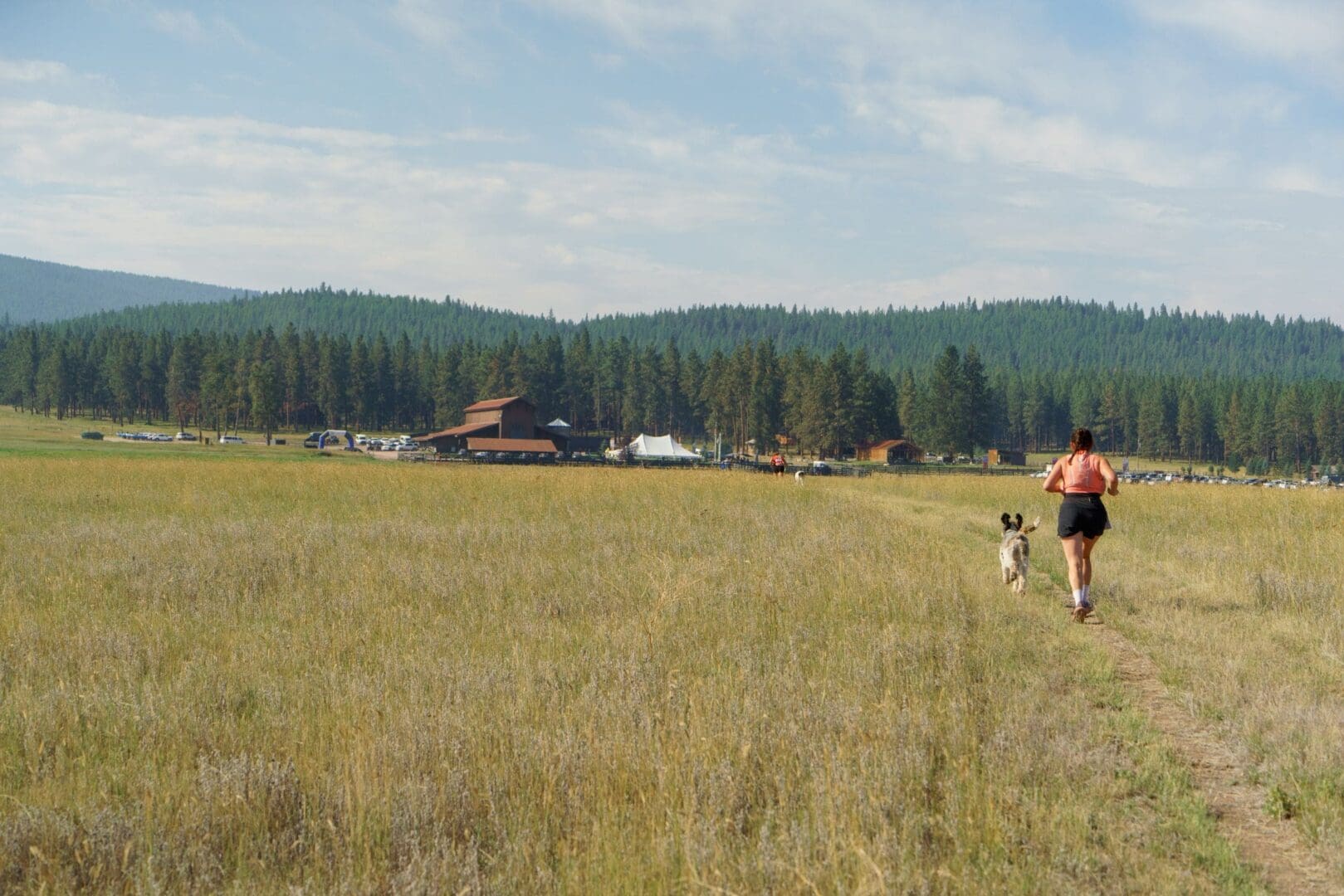 Runner with her dog traveling through a green valley at Paws Up Montana