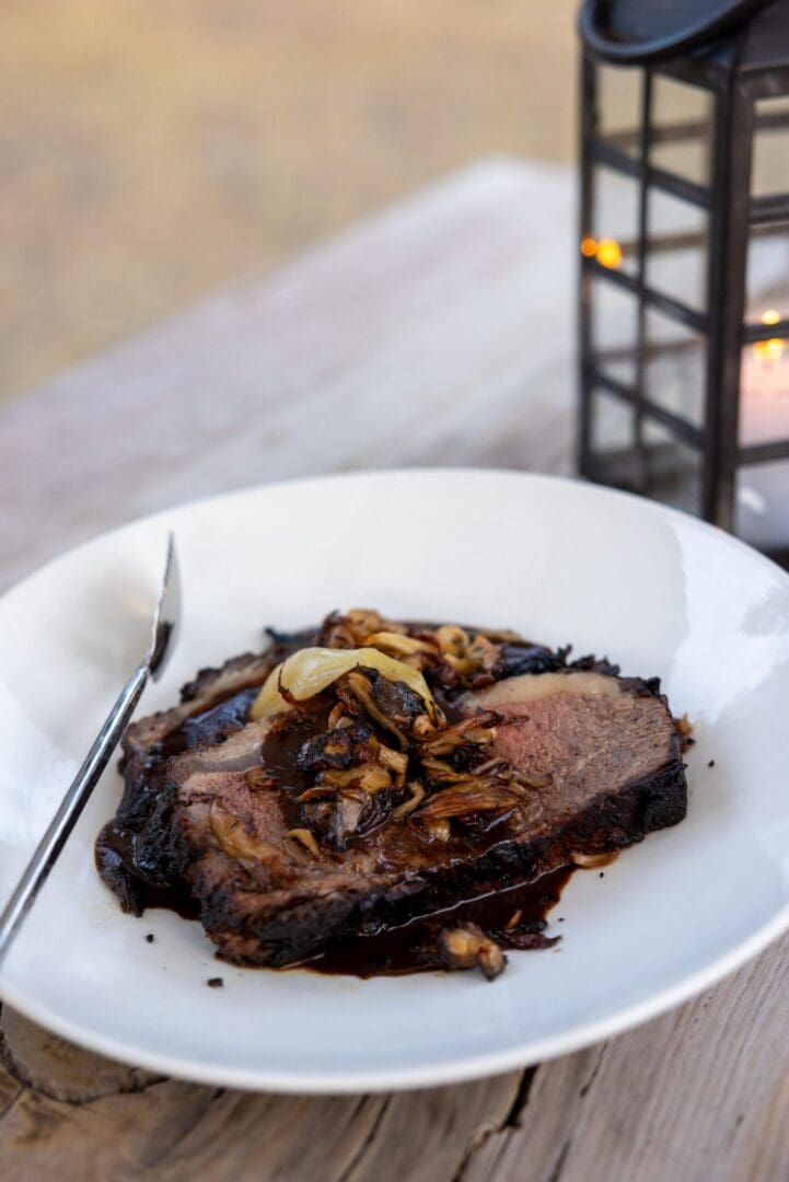 A meat dish prepared on a white plate set a top a wooden table.
