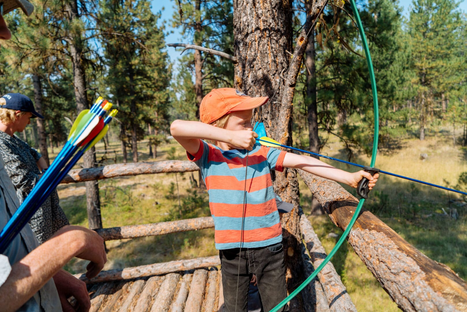 Kid shooting a bow and arrow in a forest.