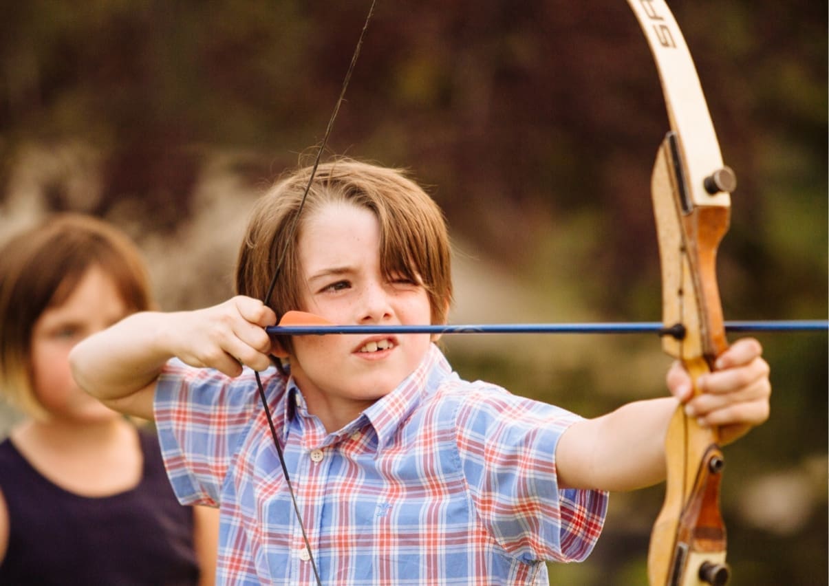little boy aiming for a target with a bow in archery
